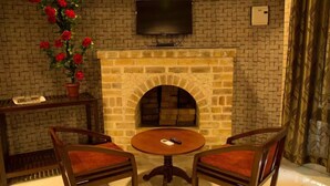 Una habitació amb una llar de pedra, televisió penjada a la paret per damunt i dos seients amb almoadins.