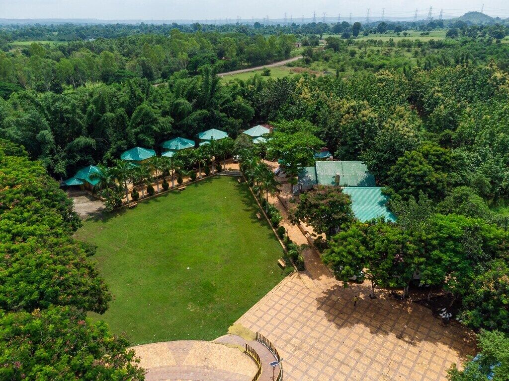 Luchtbeeld van een resort met een grasveld in het midden, omgeven door bomen en enkele gebouwen met groene daken.