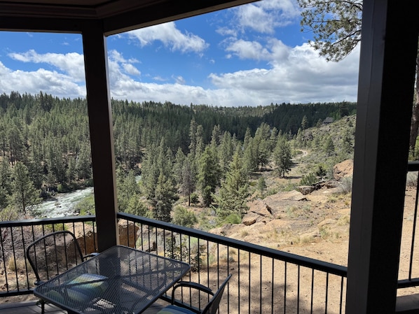 A balcony with a metal table and chairs, overlooking a forested valley with a river. - River Ridge 513AB - Best River Views! Gorgeous Mt Bachelor Village Condo (Bend)