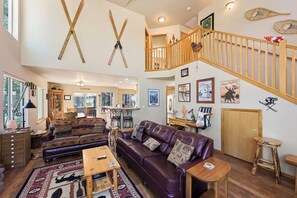 Un vaste espace de vie doté d’un haut plafond, d’un escalier en bois et de différents types de sièges, notamment un canapé en cuir et un divan à motifs.
