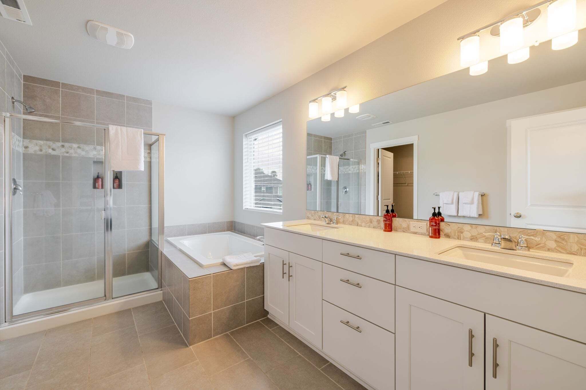 A modern bathroom with a glass-enclosed shower, a bathtub, a large mirror, and a vanity with a sink.