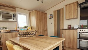 A kitchen with wooden cabinets, a microwave, a stove, and a dining table with chairs. - Morwenna (Padstow)