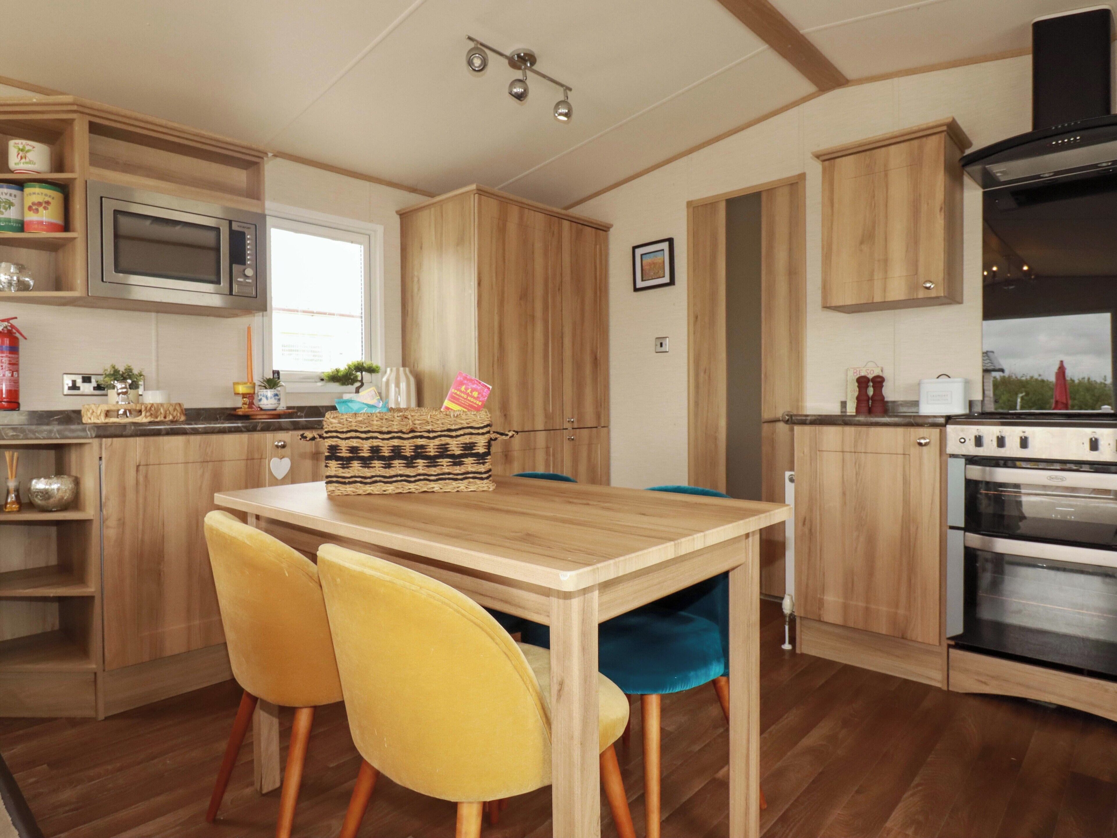 A kitchen with wooden cabinets, a microwave, a stove, and two yellow chairs.
