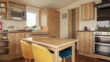 A kitchen with wooden cabinets, a microwave, a stove, and two yellow chairs.