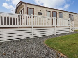A mobile home with a white exterior, a gravel driveway, and a white fence.