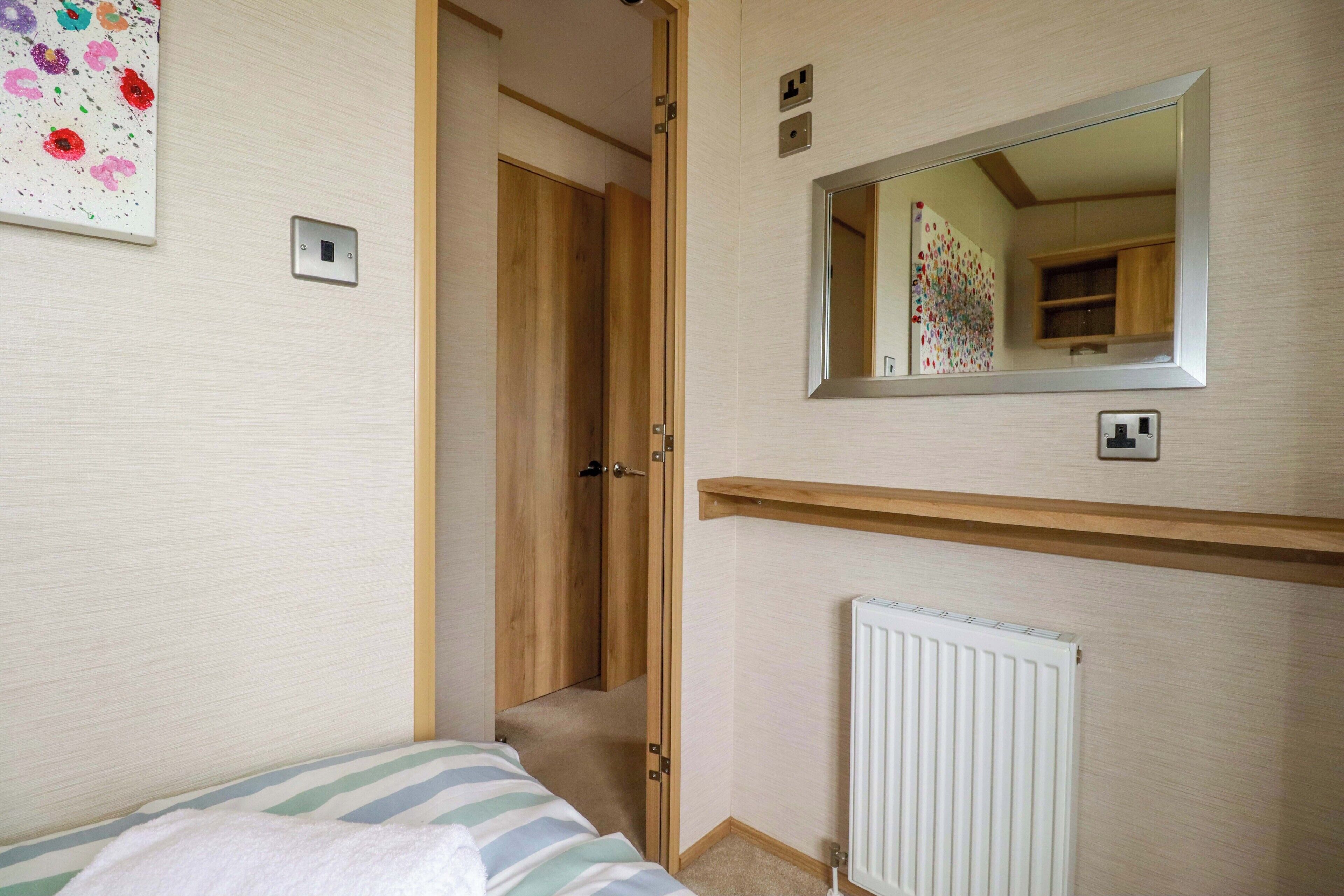 A bedroom with a bed, a wooden door, a mirror, a radiator, and a wall with a floral artwork.