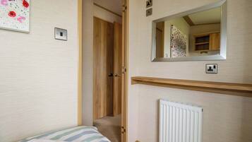 A bedroom with a bed, a wooden door, a mirror, a radiator, and a wall with a floral artwork.