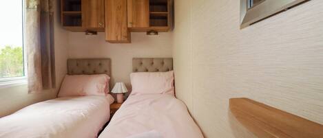 A bedroom with two beds, wooden cabinets above, a window with curtains, and a radiator.