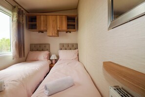 Un dormitorio con dos camas, armarios de madera arriba, una ventana con cortinas y un radiador.
