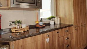 A kitchen with wooden cabinets, a microwave, a window, and a small potted plant on the counter. - Morwenna (Padstow)