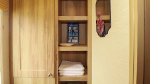 A wooden cabinet with a blue sign, a folded white towel, and a mirror with a floral decoration. - Morwenna (Padstow)