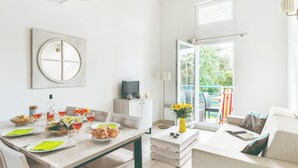 A modern, well-lit room with a dining table set for two, a sofa, a TV, and a balcony with outdoor seating. - Duplex Coastal Escape (Saint-Palais-sur-Mer)