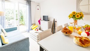 A bright room with a dining table, a sofa, a surfboard, and a TV. - Duplex Coastal Escape (Saint-Palais-sur-Mer)
