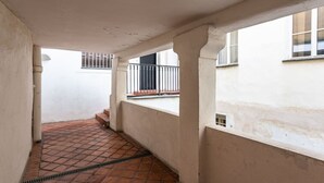 A narrow corridor with tiled flooring, white walls, and a window with a metal railing.