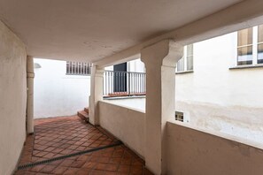 Un estrecho pasillo con piso de baldosas, paredes blancas y una ventana con barandilla metálica.