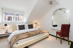 Ein Schlafzimmer mit Bett, einem roten Sessel, einem Fenster mit Jalousien und einem Wandspiegel.