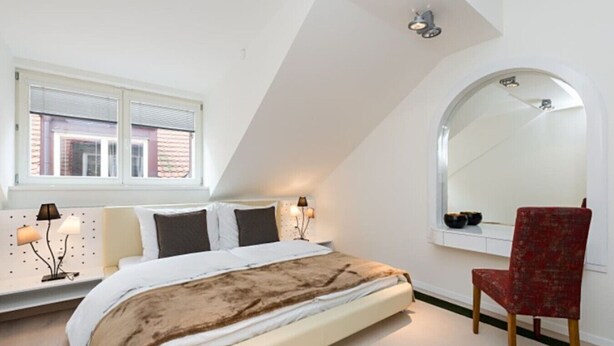 A bedroom with a bed, a chair, a window, and a mirror.