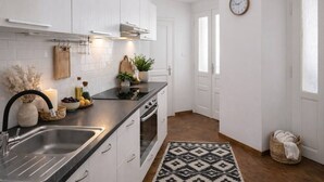 Een moderne keuken met witte kastjes, een zwart aanrecht, een roestvrijstalen spoelbak en een ingebouwde oven, plus een klok aan de muur.
