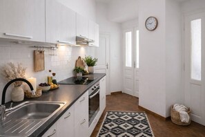 Eine moderne Küche mit weißen Schränken, einer schwarzen Arbeitsplatte, einer Edelstahlspüle, einem eingebauten Backofen und einer Uhr an der Wand.