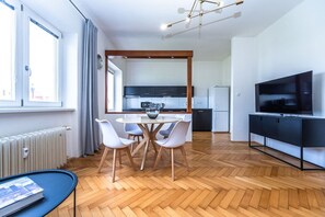 A modern kitchen with dark cabinets, a white refrigerator, and a dining area with a round table and white chairs. - Urban Elegance Residence in Smíchov (Prague 5)
