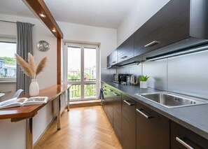 A modern kitchen with a large window, wooden flooring, and stainless steel appliances. - Urban Elegance Residence in Smíchov (Prague 5)