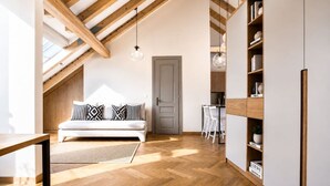 Una stanza in stile loft con soffitto in legno, un divano con cuscini decorati, un'area pranzo con sedie e una libreria.