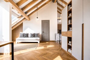Ein Loft-Zimmer mit Holzbalkendecke, einer Couch mit gemusterten Kissen, einem Essbereich mit Stühlen und einem Bücherregal.