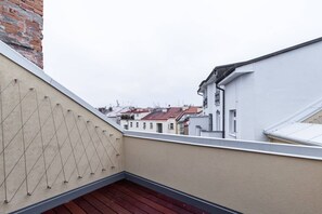 Eine Dachterrasse mit Blick auf benachbarte Gebäude, einem Metallgeländer und einem Holzboden.