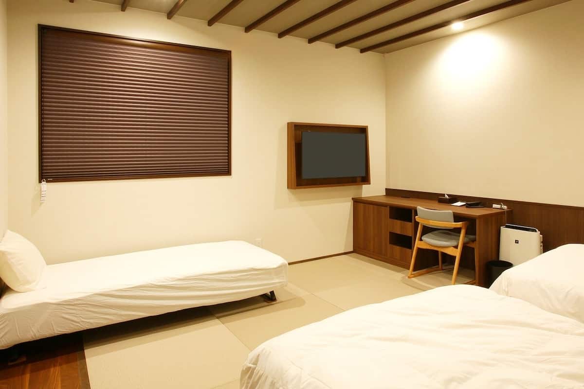 A hotel room with two beds, a desk, a chair, a TV, and a waste bin.