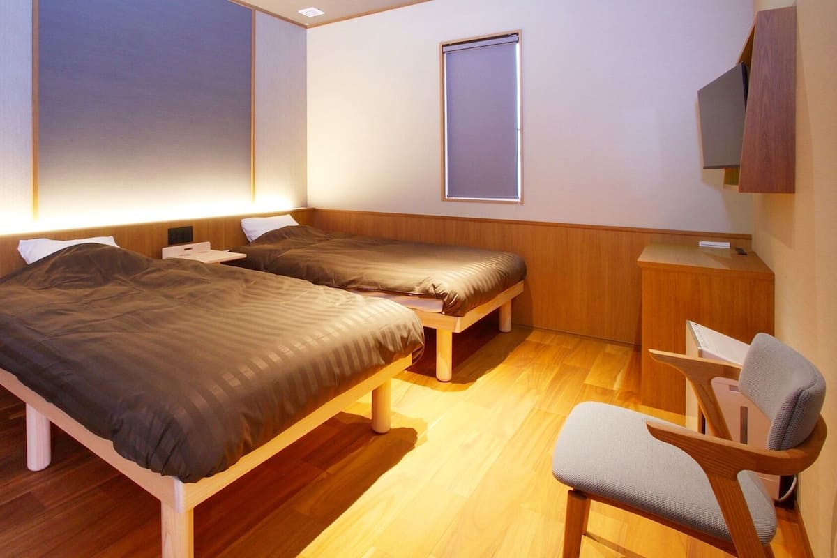 A room with two beds, a desk, a chair, and a window.