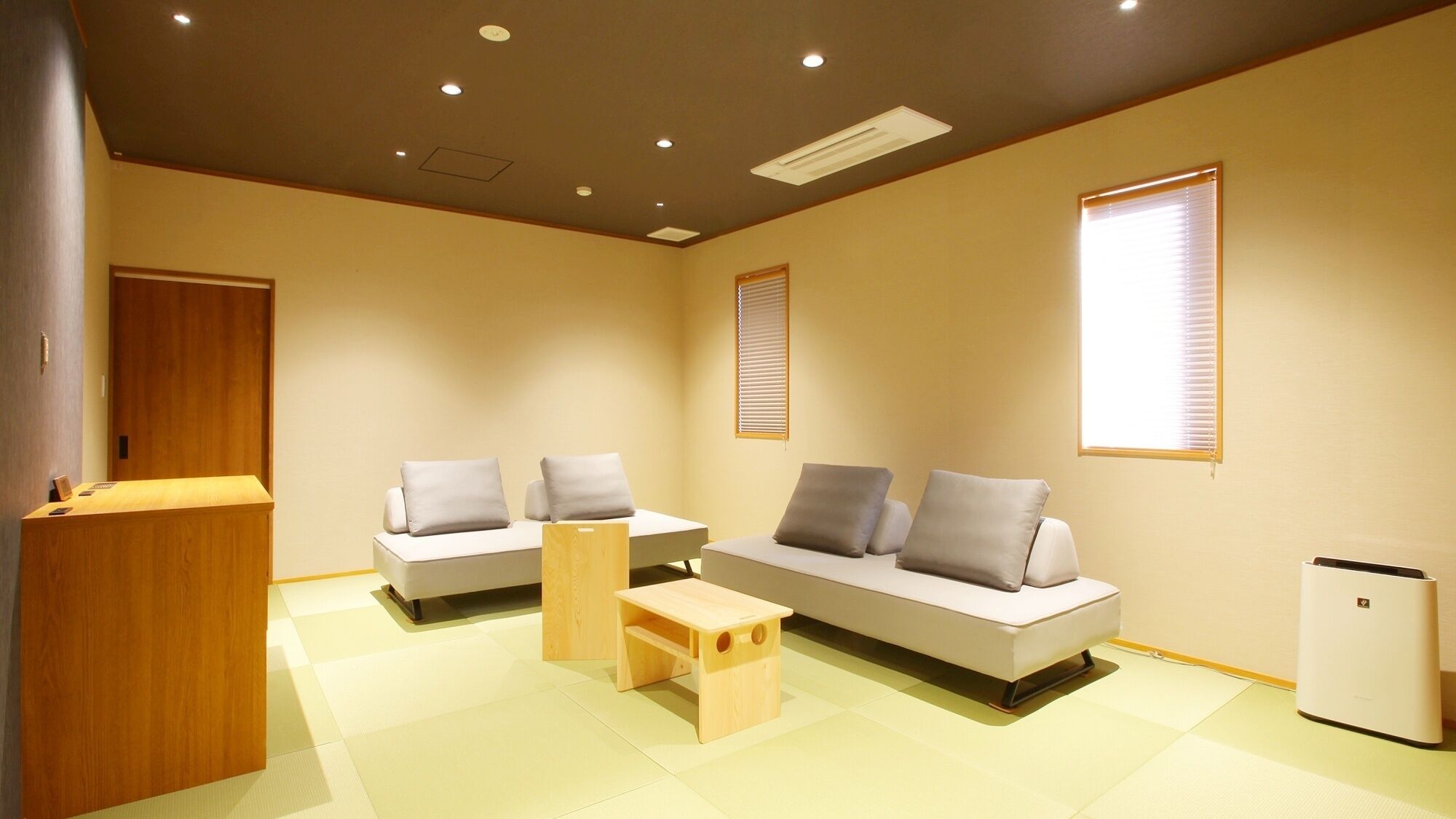 Uma sala de estar moderna com um sofá, uma mesa lateral de madeira, um banquinho de madeira pequeno, uma geladeira branca e uma porta de madeira.
