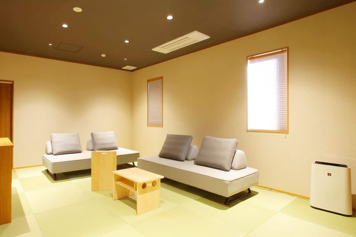 A modern living room with a sofa, a wooden side table, a small wooden stool, a white refrigerator, and a wooden door.