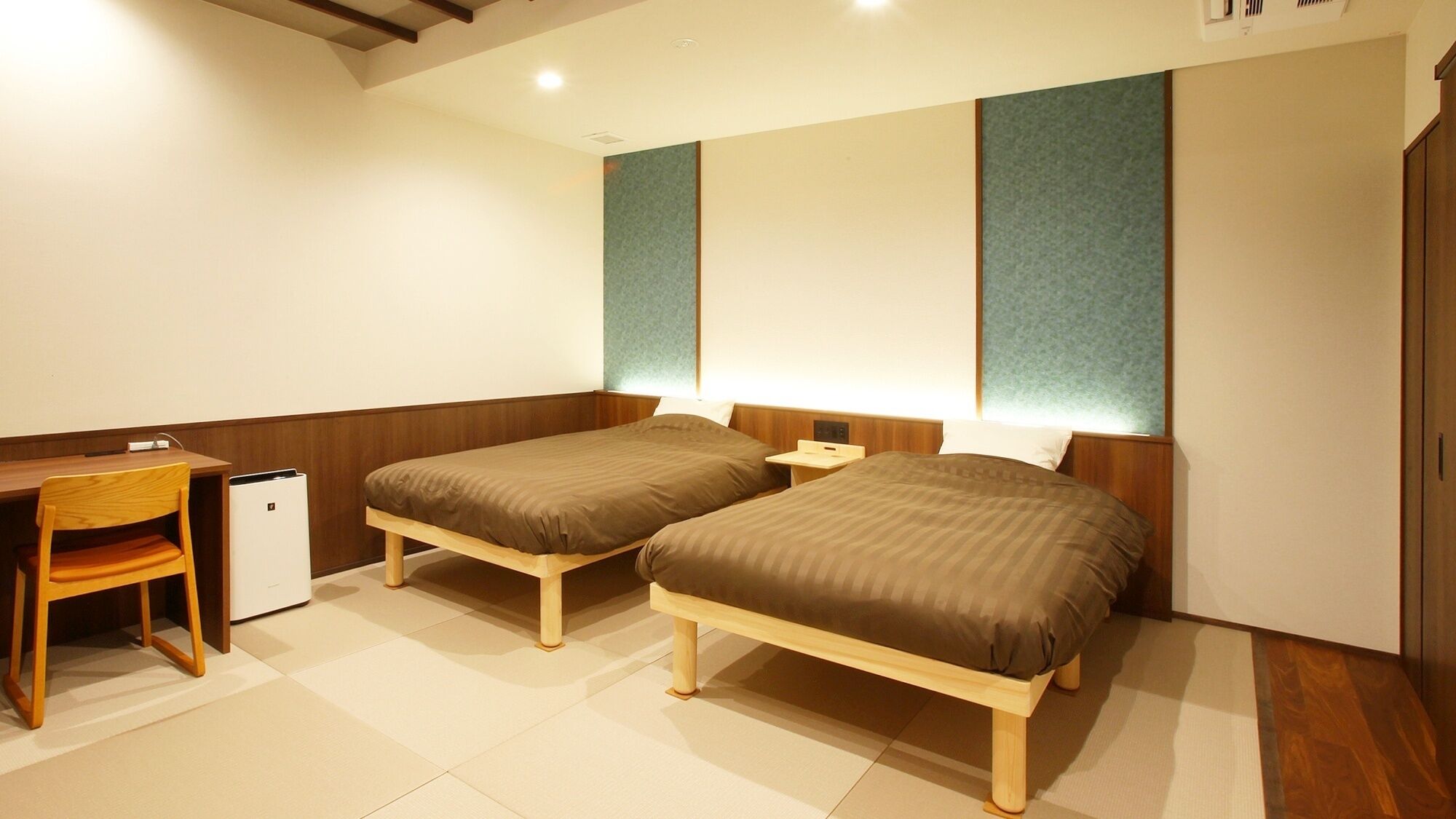 Quarto de hotel com duas camas de solteiro, uma escrivaninha, uma cadeira e um pequeno frigorífico.