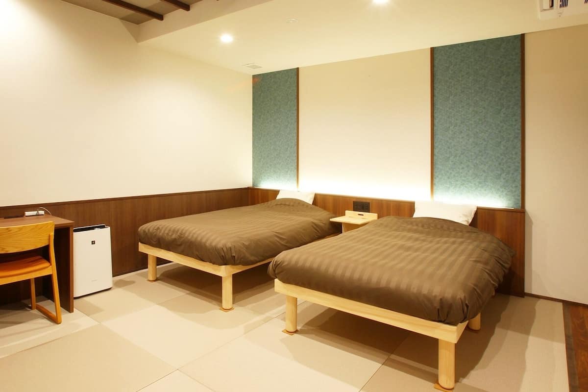 A hotel room with two single beds, a desk, a chair, and a small refrigerator.