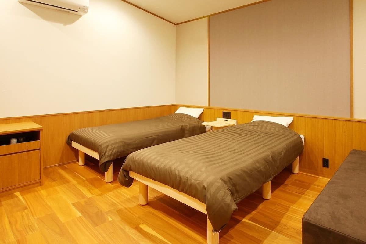 A room with two single beds, a wooden bench, a small table, and a wall-mounted air conditioner.