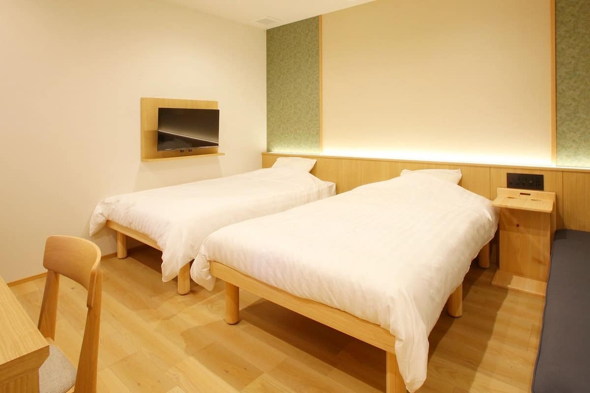 A hotel room with two beds, a desk, and a chair.