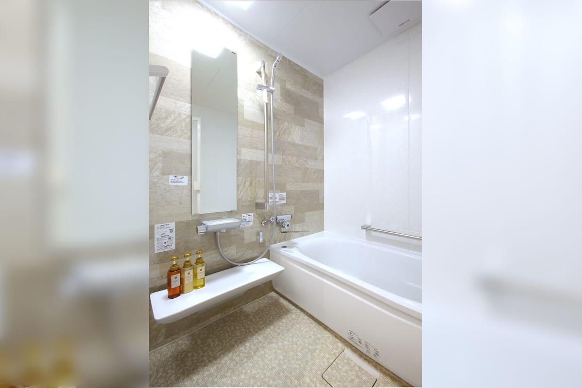 A bathroom with a bathtub, a shower, a mirror, and a shelf with toiletries.