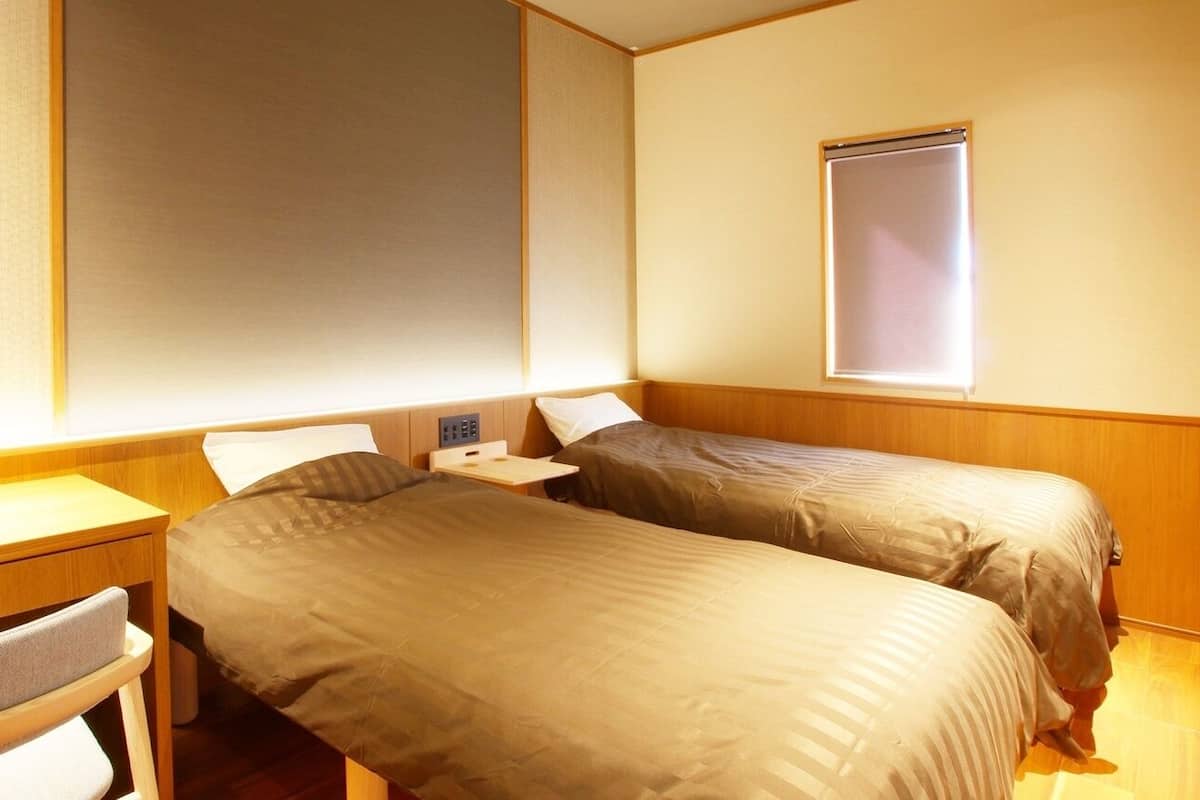 A room with two beds, a small desk, and a window.