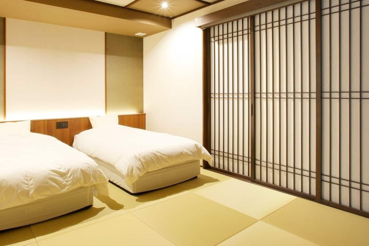 A room with two beds, a sliding shoji screen, tatami flooring, and a wooden headboard.