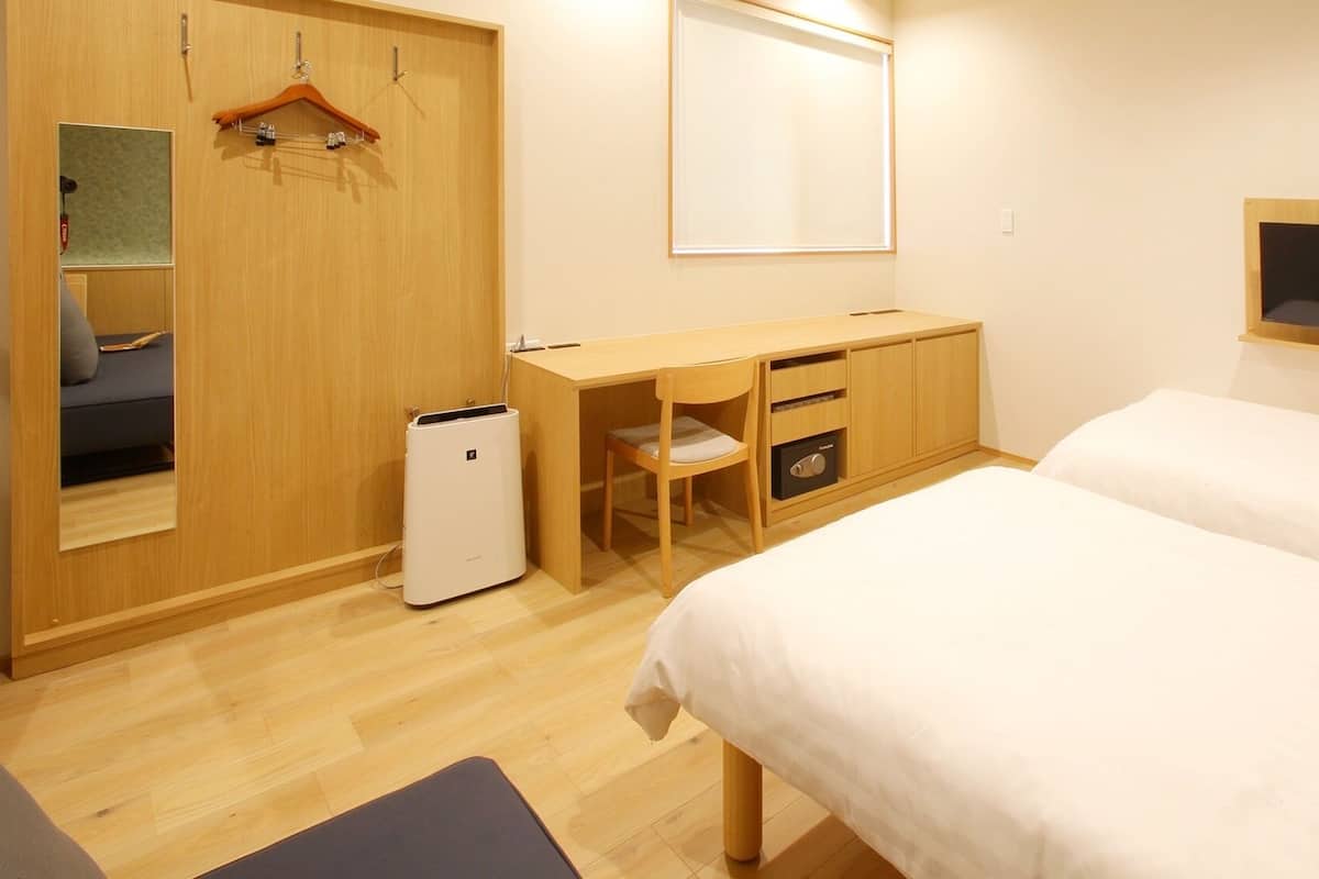 A hotel room with a wooden desk, two beds, a small refrigerator, a mirror, and a TV.