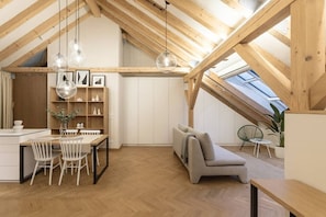 A loft-style room with a wooden ceiling, a dining area with a table and chairs, a sofa, and a small balcony with a plant. - Cozy Attic Loft with Terrace in Prime Location (Prague 2)
