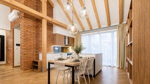 Een moderne keuken met een bakstenen muur, houten balken en een eethoek met een tafel en stoelen.