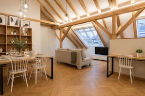Ein modernes Loft mit freiliegenden Holzbalken, einem Essbereich mit weißen Stühlen, einer Couch und einem Fernseher auf einem Holztisch.