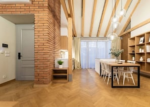 A modern kitchen with wooden flooring, a brick accent wall, and a dining area with white chairs and a wooden table. - Cozy Attic Loft with Terrace in Prime Location (Prague 2)