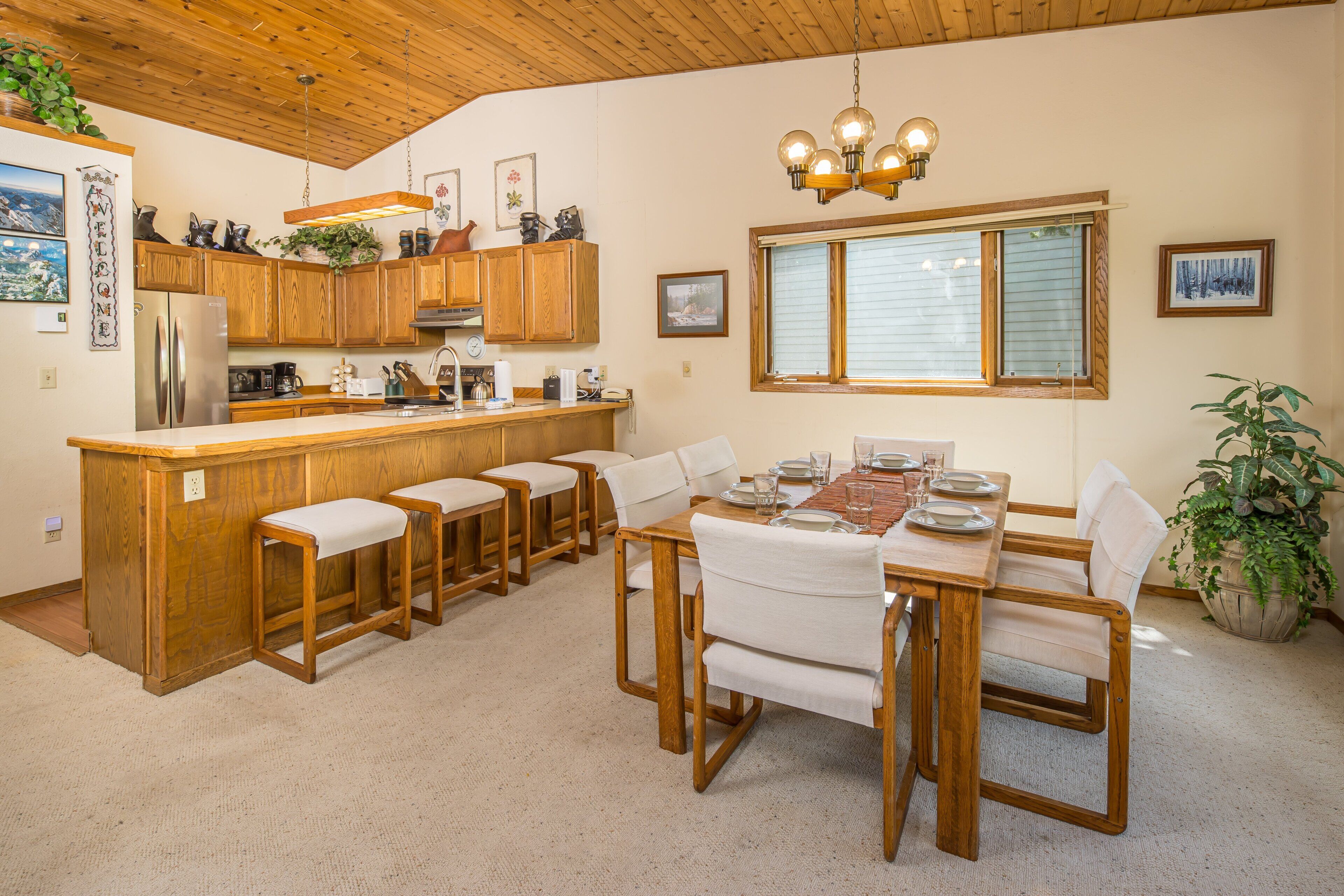 A kitchen with wooden cabinets, a stainless steel refrigerator, and a bar area with stools.