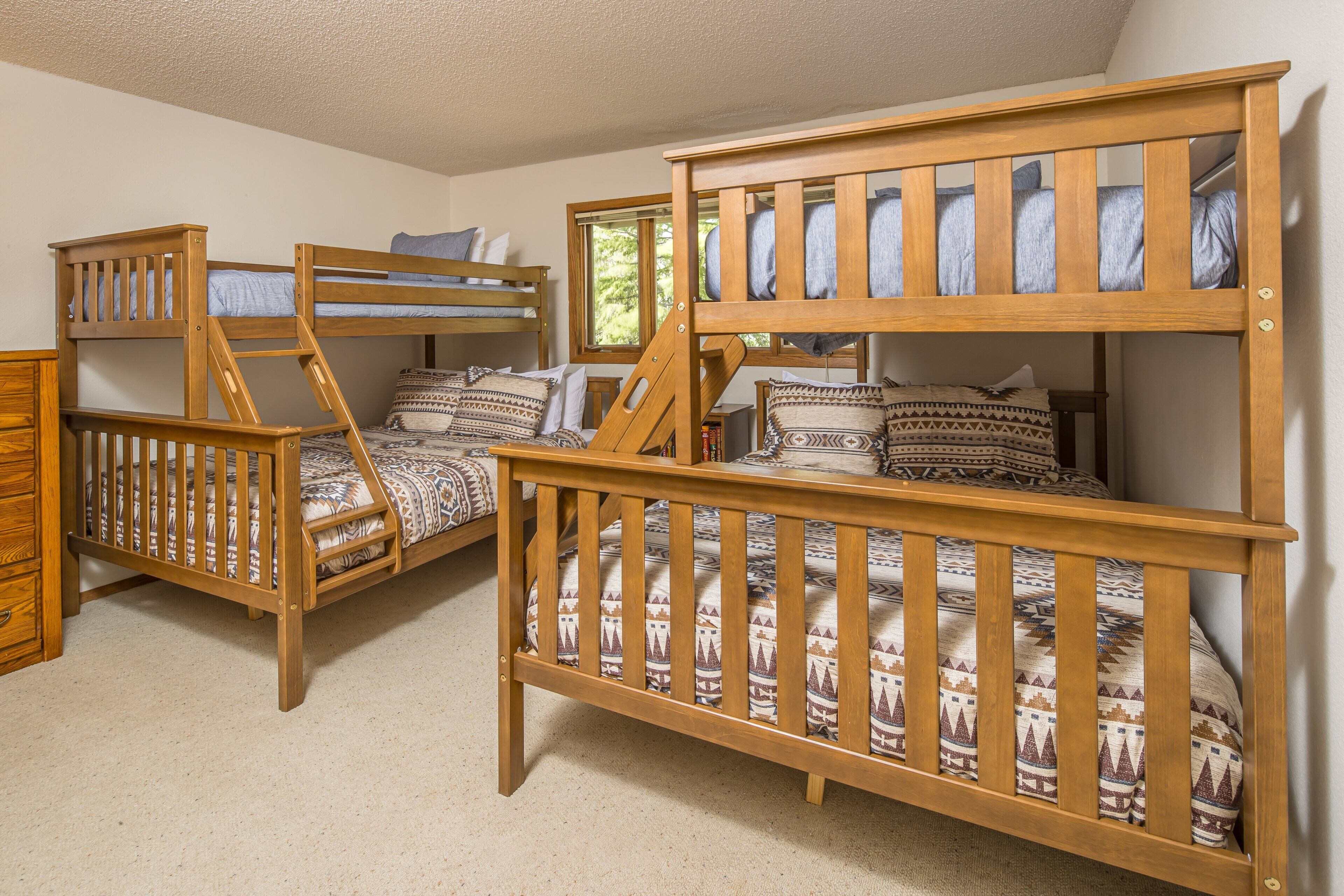 A room with three wooden bunk beds, a wooden dresser, and a window with a view of trees.