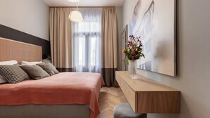 A modern bedroom with a bed, a bedside table, a chair, a desk, and a window with curtains. - Stylish Residence in Parkside Vinohrady (Prague 2)