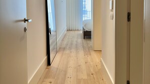 Un pasillo con suelo de madera, paredes blancas y una cama al fondo.