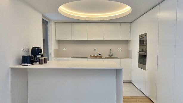Una cocina moderna con una isla central, electrodomésticos integrados e iluminación empotrada en el techo.