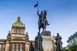 Eine Statue eines rittenden Mannes mit einer Flagge, ein Gebäude mit einer Kuppel und eine weitere Statue im Vordergrund.